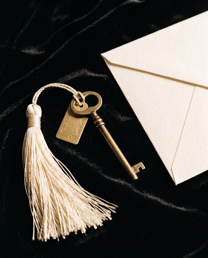 An antique brass key with an ivory tassel beside an envelope