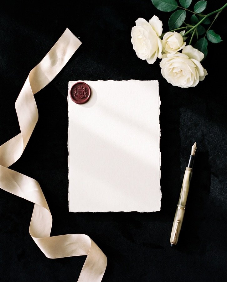 An ivory letterpress invitation with a bordeaux wax seal on black velvet